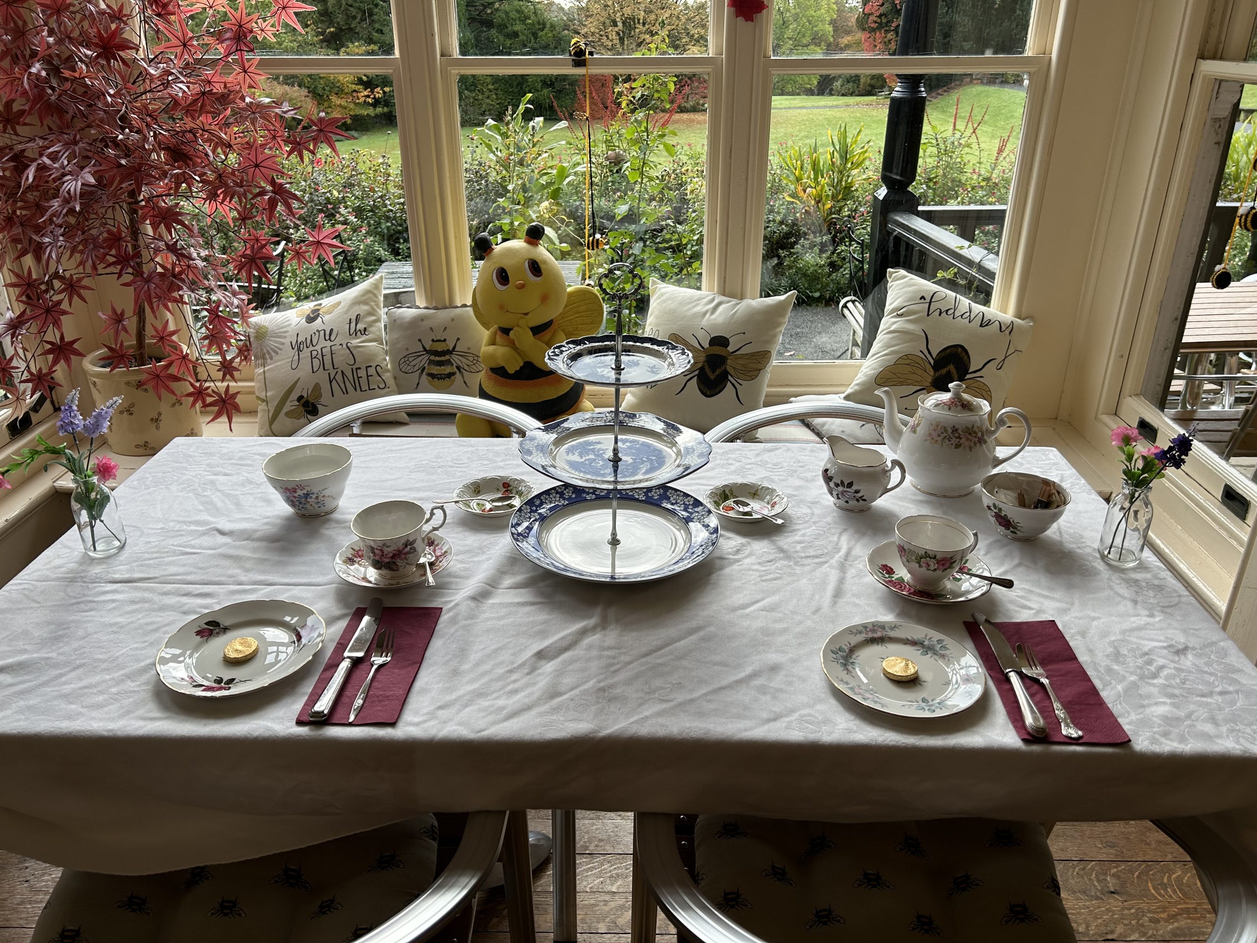 a table with cutlery, cups, teapots and trays for afternoon tea on a table with a window behind providing a view of the gardens